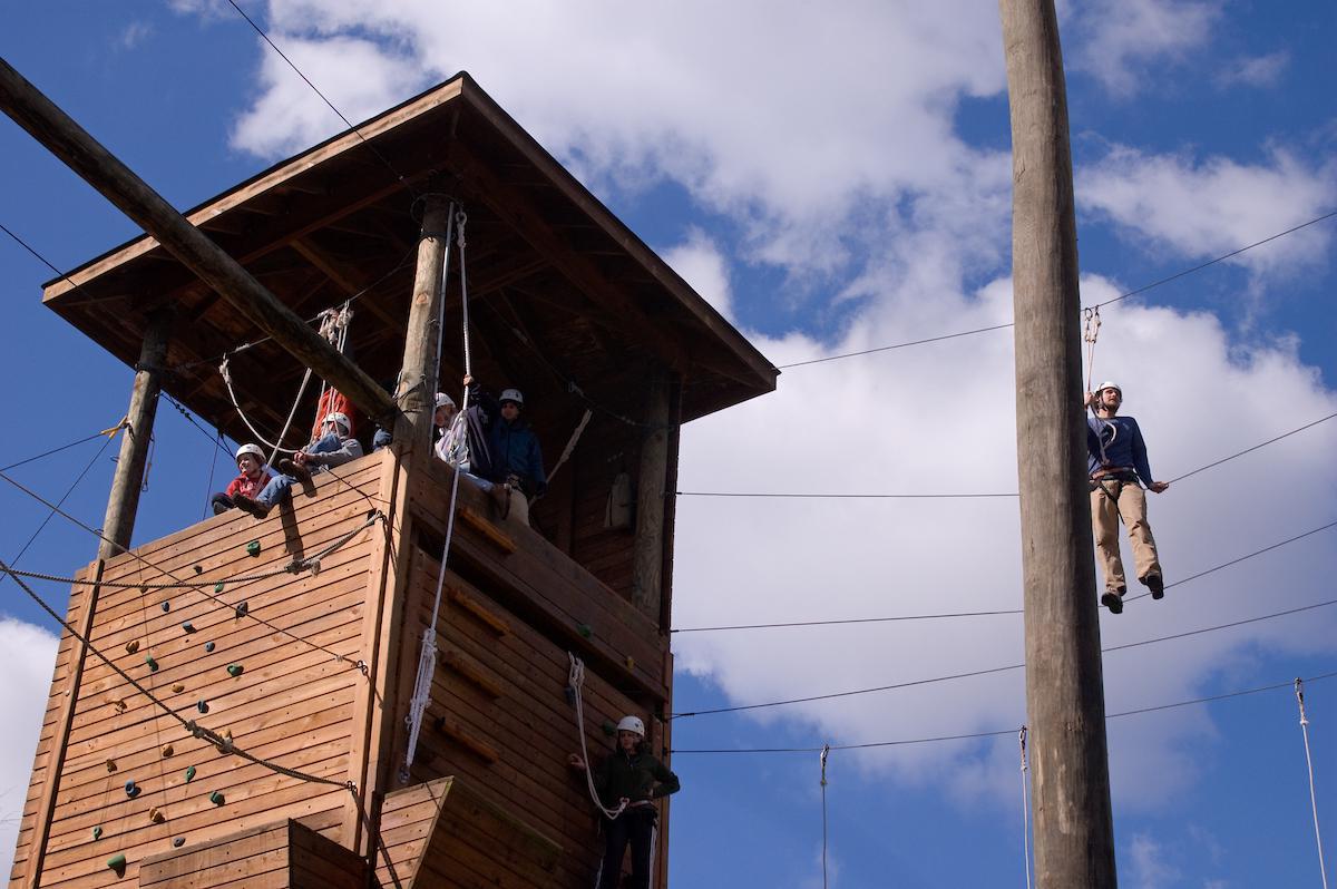 Students sit in a high ropes course tower, atop a rock wall at bet8九州登录入口